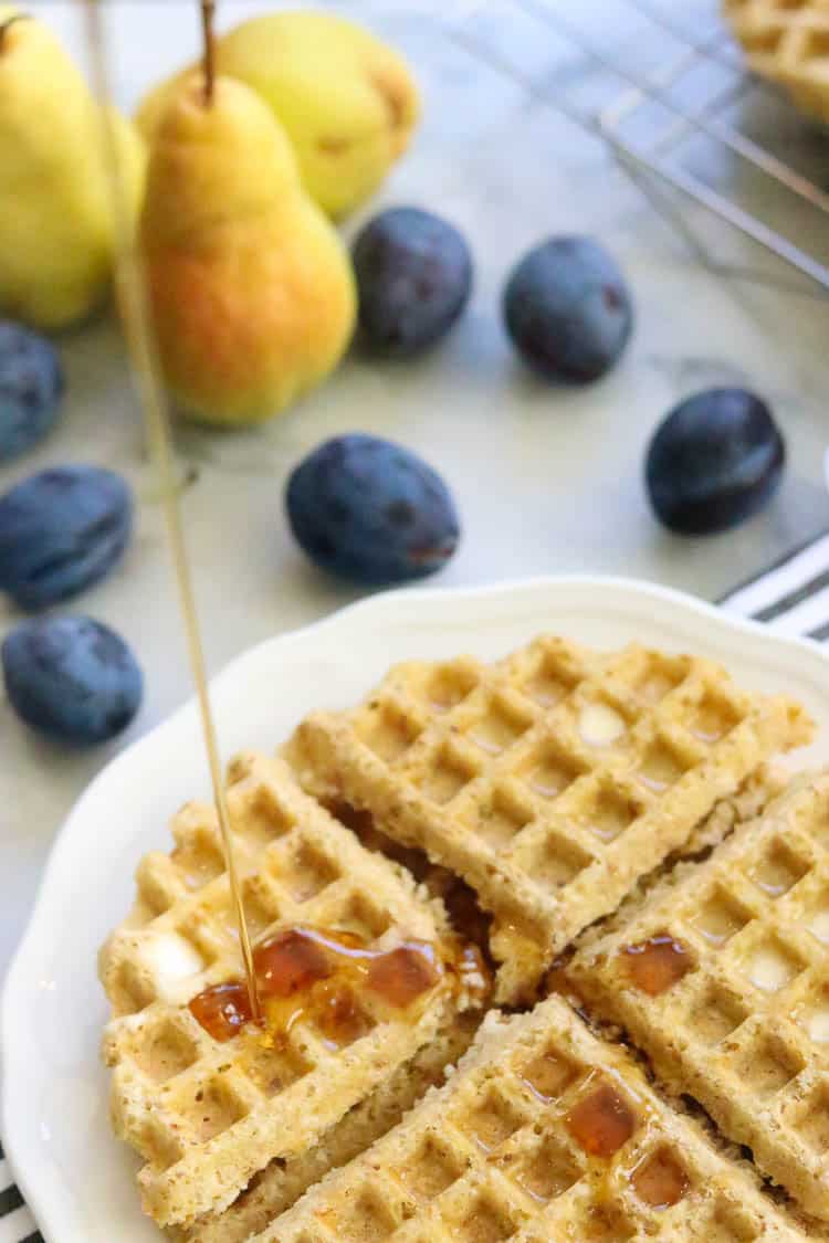 overhead shot of vegan waffles quartered on white plate with maple syrup being drizzled over