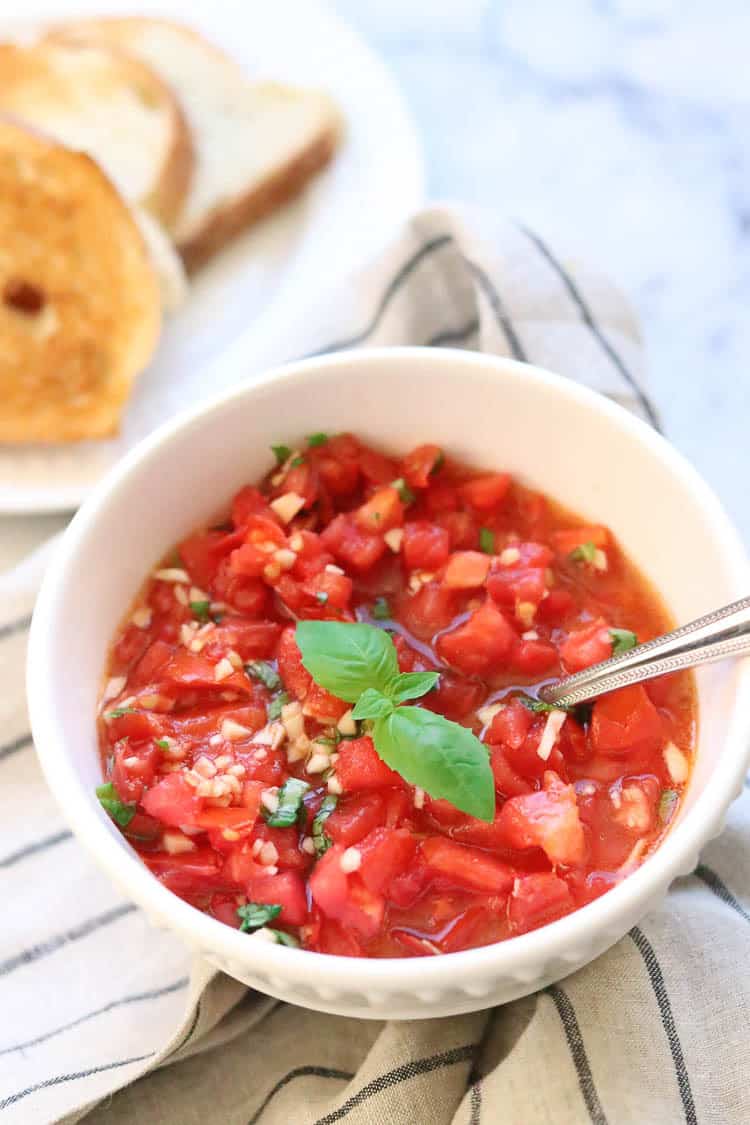 side overhead shot of bruschetta in white bowl with striped napkin and toast in the background