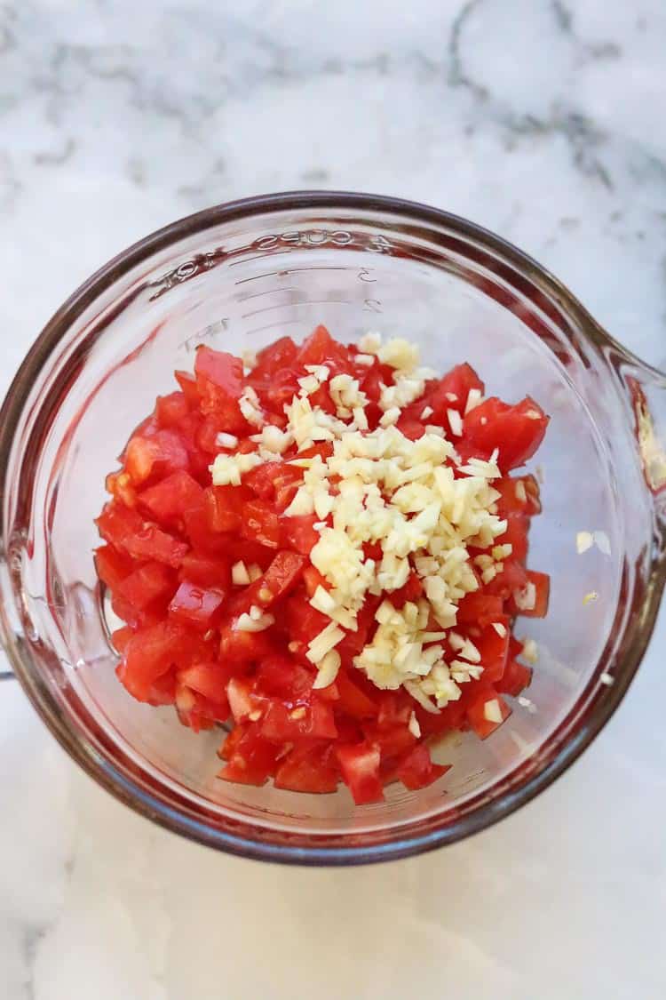overhead shot of finely diced tomatoes and chopped garlic in a mixing bowl