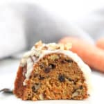 side closeup shot of vegan carrot cake sliced on a white plate with carrots in background
