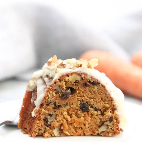 side closeup shot of vegan carrot cake sliced on a white plate with carrots in background