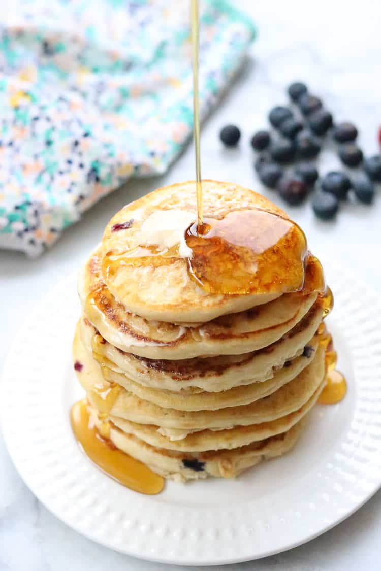  maple syrup being poured over a tall stack of vegan buttermilk pancakes