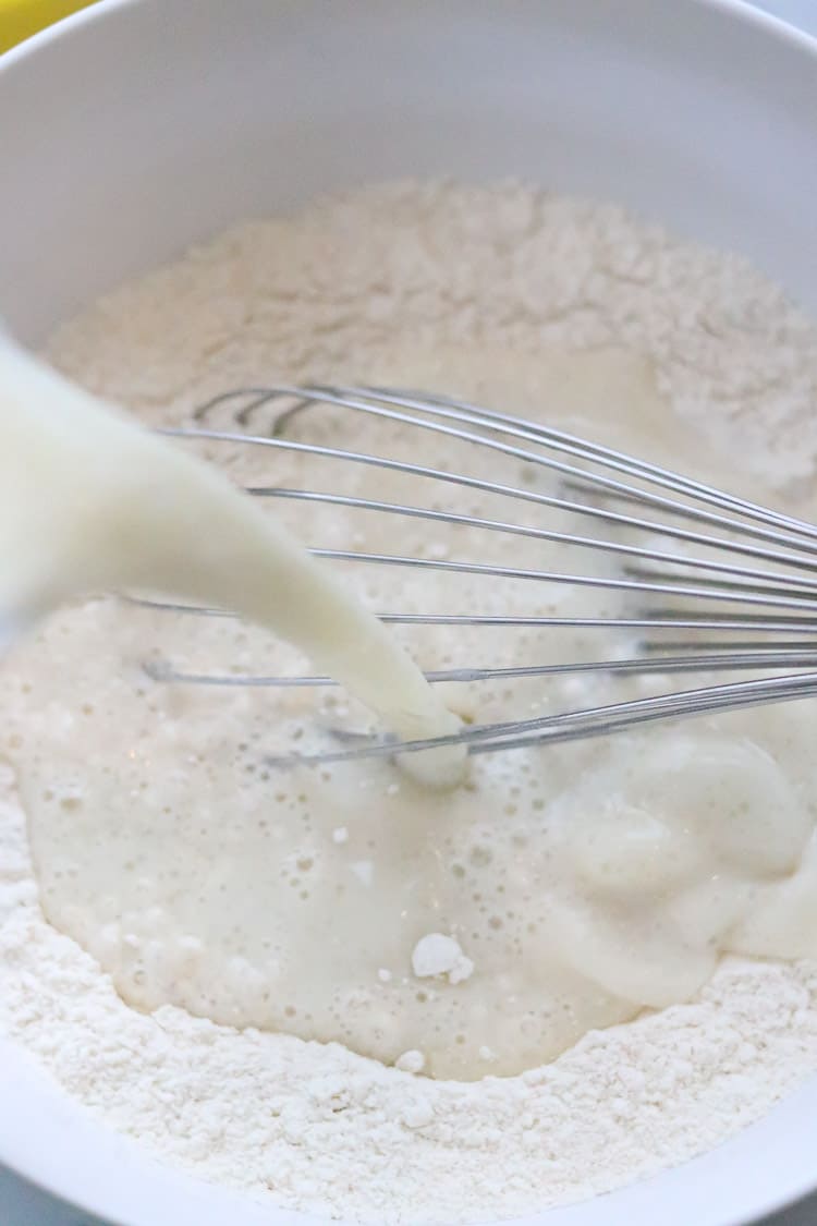 vegan buttermilk being poured into vegan pancake mixture in a bowl with a whisk