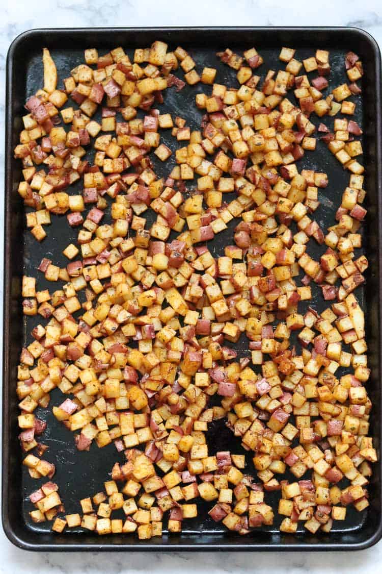 overhead shot of baked diced breakfast potatoes on a dark baking sheet