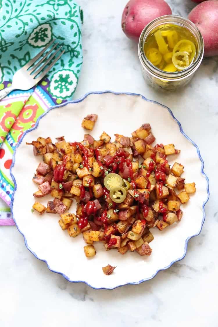 wide overhead shot of baked breakfast potatoes on a white plate with jalapeño slices and ketchup