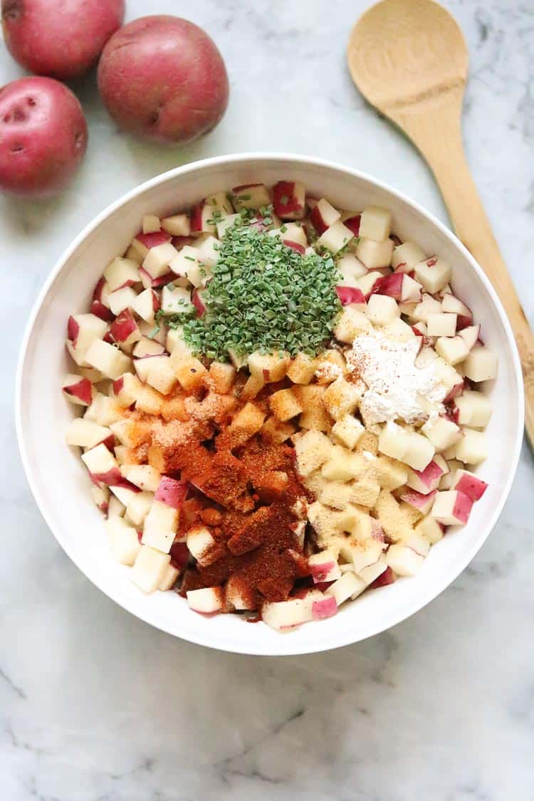 diced breakfast potatoes in a white bowl with seasonings on top and wooden spoon beside