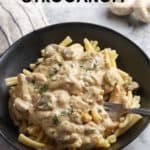 side overhead photo of stroganoff in a black pasta bowl with fork in dish and mushrooms and napkin nearby