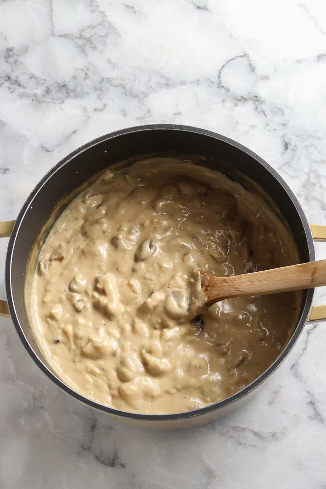 overhead photo of thickened mushroom stroganoff in a dutch oven with wooden spoon