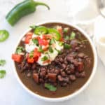 overhead photo of a white bowl filled with black bean soup and garnished with sour cream and pico de gallo