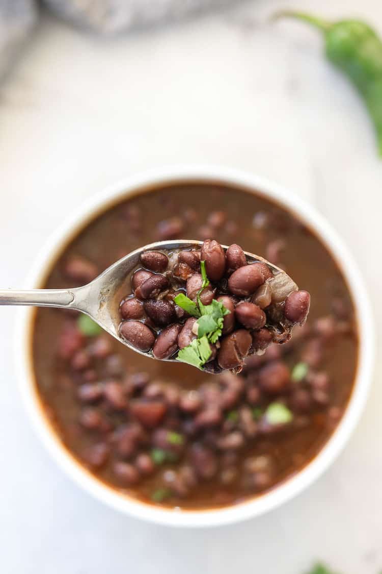 overhead photo of silver spoon holding black bean soup with cilantro garnish