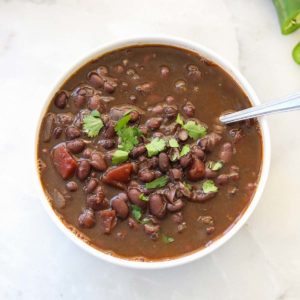 overhead shot of black bean soup in a white bowl with a garnish of chopped cilantro