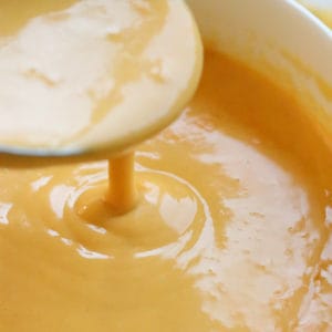 vegan nacho cheese sauce on a spoon being poured into a bowl