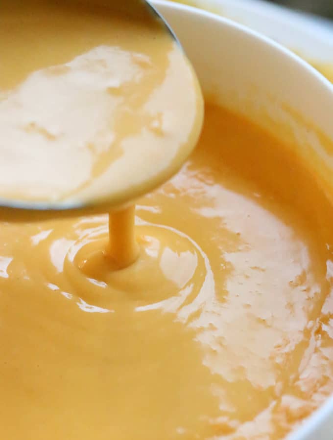 vegan nacho cheese sauce on a spoon being poured into a bowl