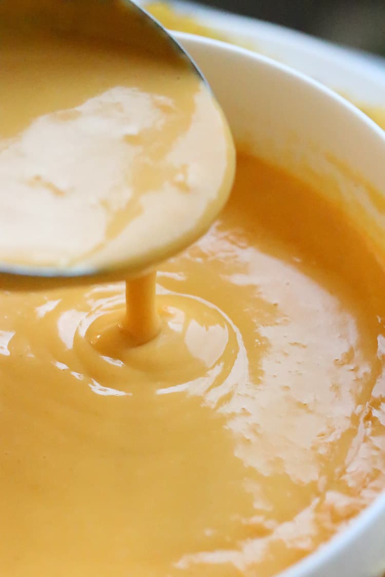 cheese sauce pouring from a spoon into a white bowl.