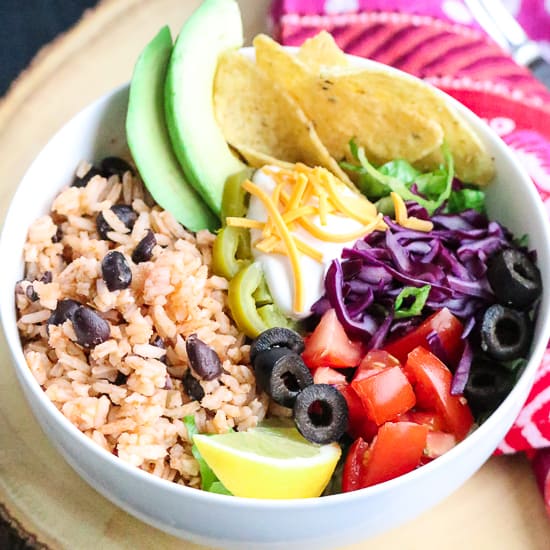 Napkin place beside white bowl filled with Vegan Mexican Rice and Black Beans and other toppings.