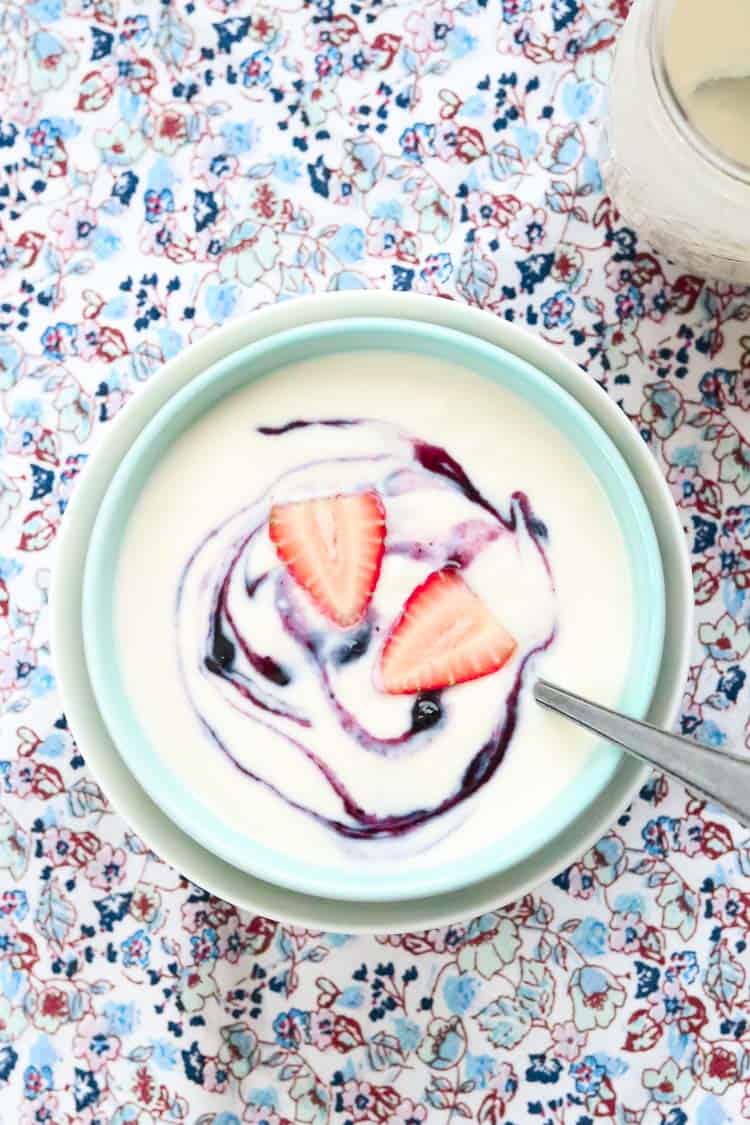 overhead shot of vegan yogurt in a double bowl with silver spoon resting on a flowered background