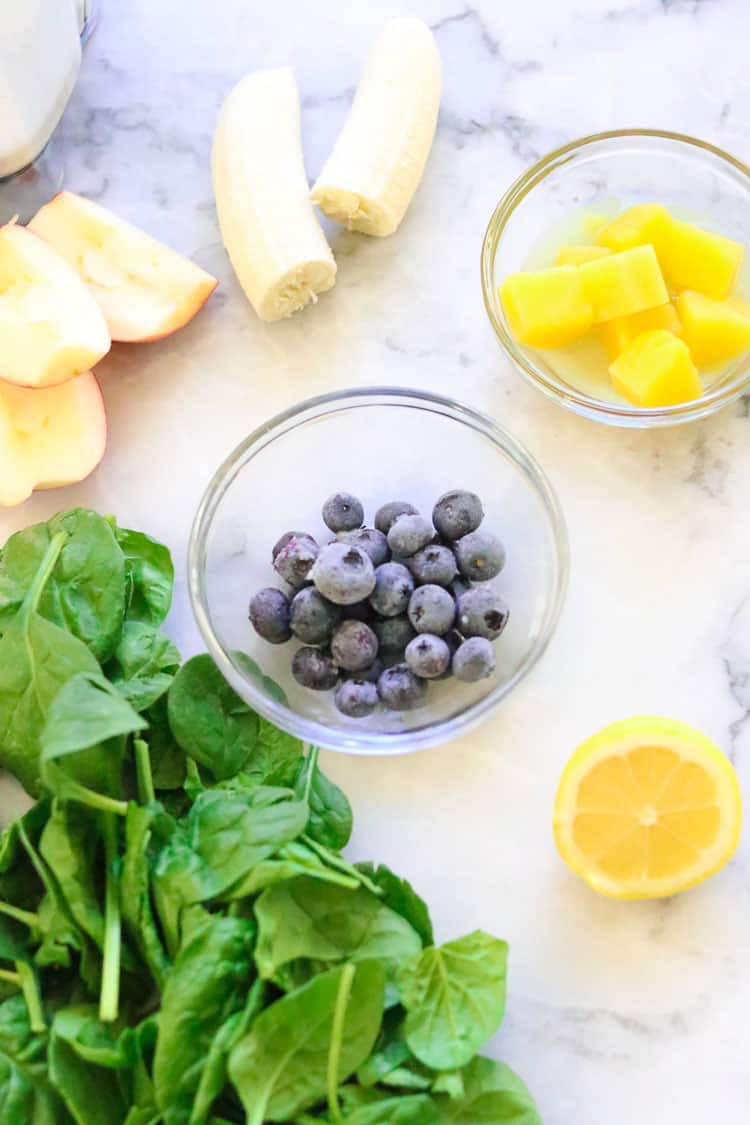 overhead shot of green smoothie ingredients in clear bowls and on marble backdrop