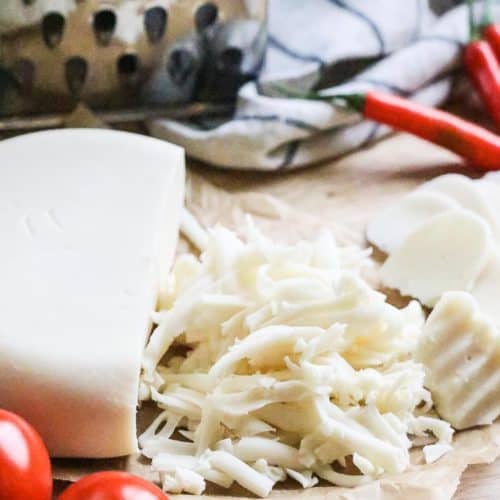 overhead view of vegan mozzarella shredded with block beside on parchment paper