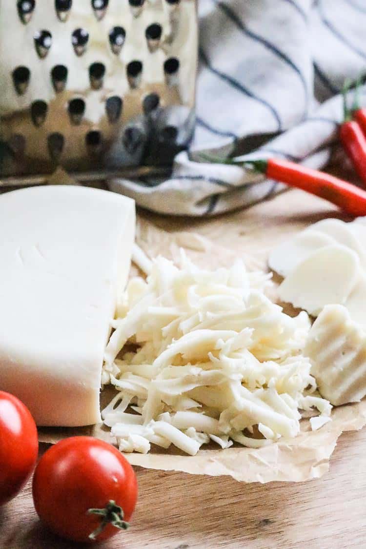 side view of vegan mozzarella cheese sliced and grated with red peppers and tomatoes beside.