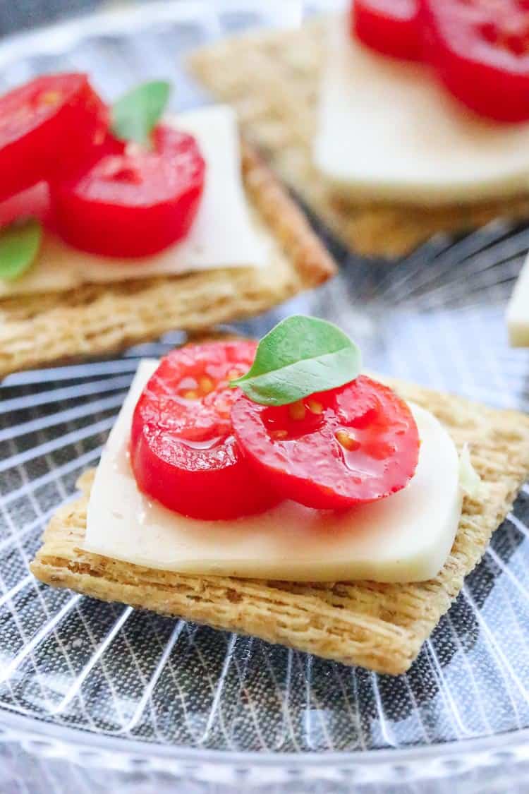  sliced vegan mozzarella cheese on a cracker with tomato slices and a basil leaf.