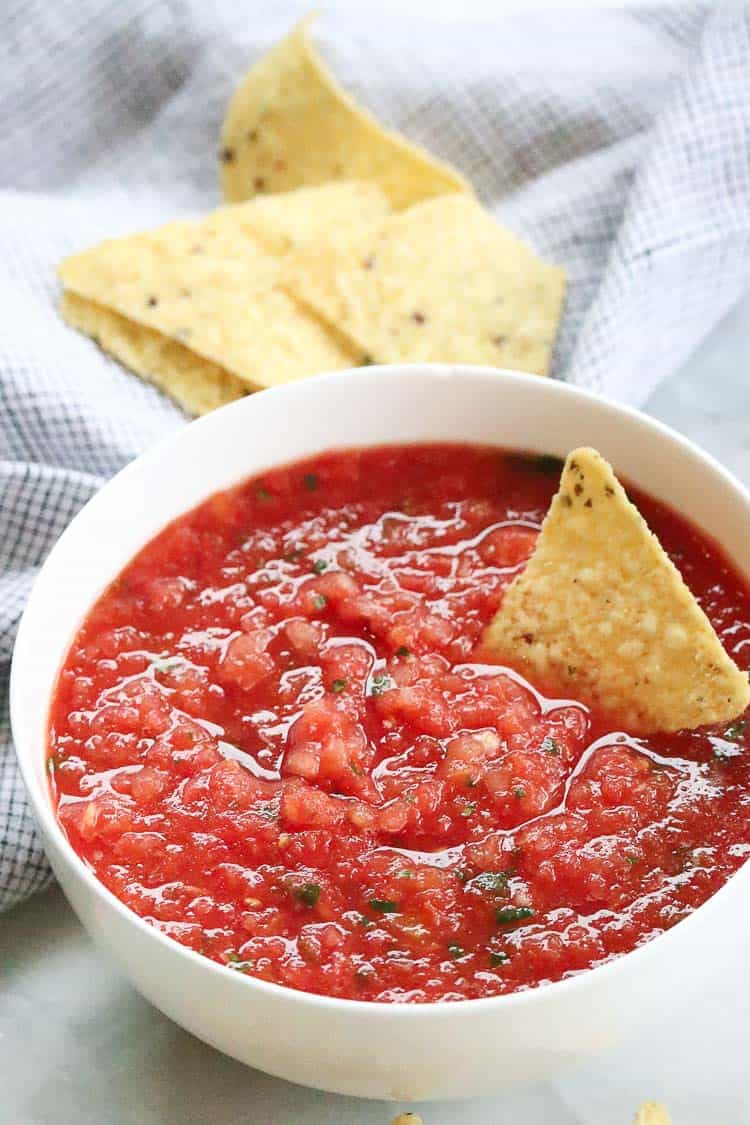 side overhead shot of salsa in a white bowl with a corn chip dipped in it