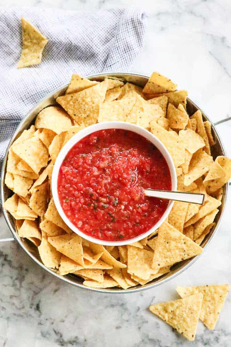 overhead photo of salsa in white bowl with chips surrounding