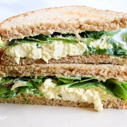 close up image of a vegan egg salad sandwich made with mashed tofu, cut in triangles and stacked on top of each other