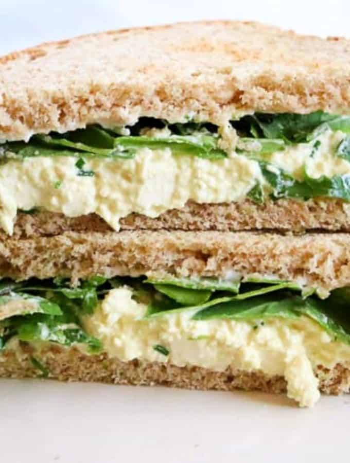 close up image of a vegan egg salad sandwich made with mashed tofu, cut in triangles and stacked on top of each other