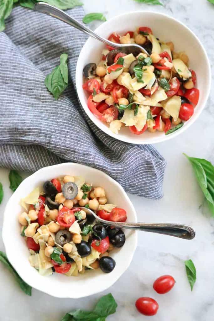 two bowls of artichoke salad with grape tomatoes, and basil leaves as a garnish