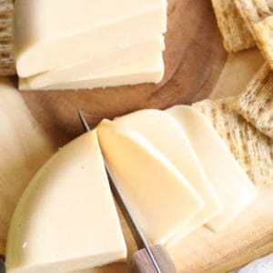 overhead shot of vegan good cheese being sliced with crackers beside