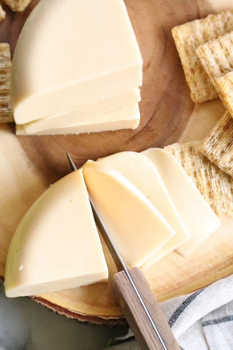 overhead shot of vegan good cheese being sliced with crackers beside