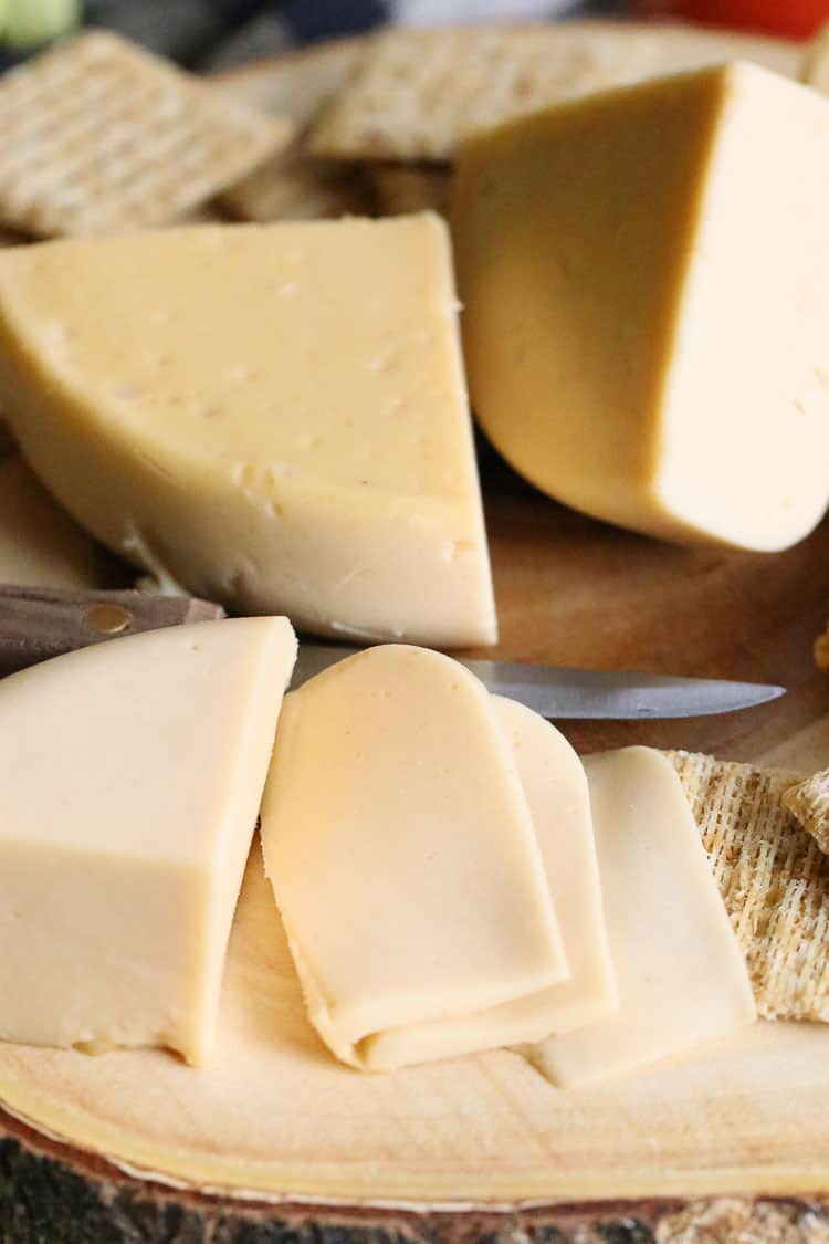 side closeup view of vegan smoked gouda cheese sliced and quartered with crackers nearby