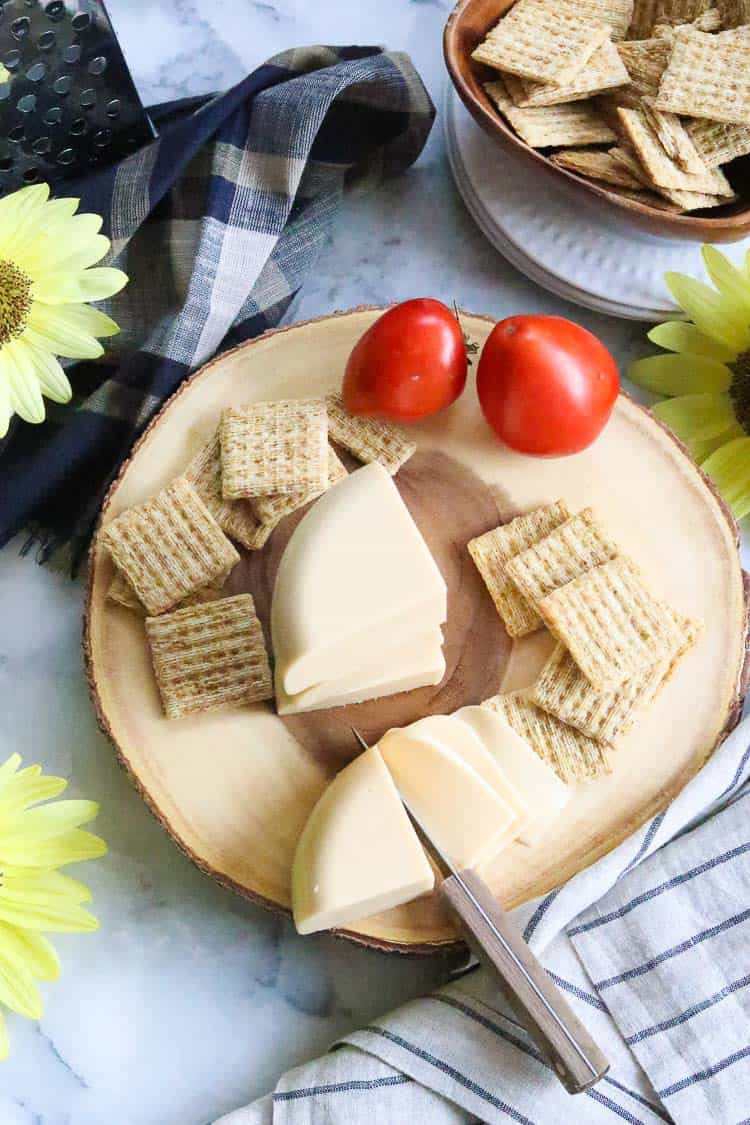 distance overhead shot of vegan smoked gouda cheese on a log board with tomatoes and sunflowers nearby