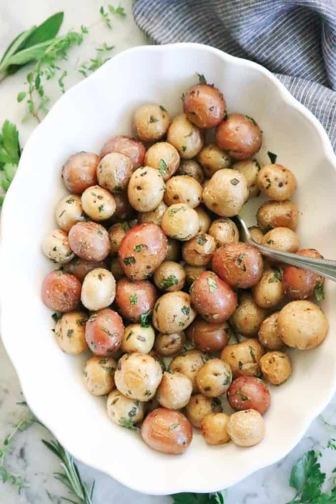 White serving dish filled with baby roasted potatoes white and red with green herbs and a napkin surrounding.