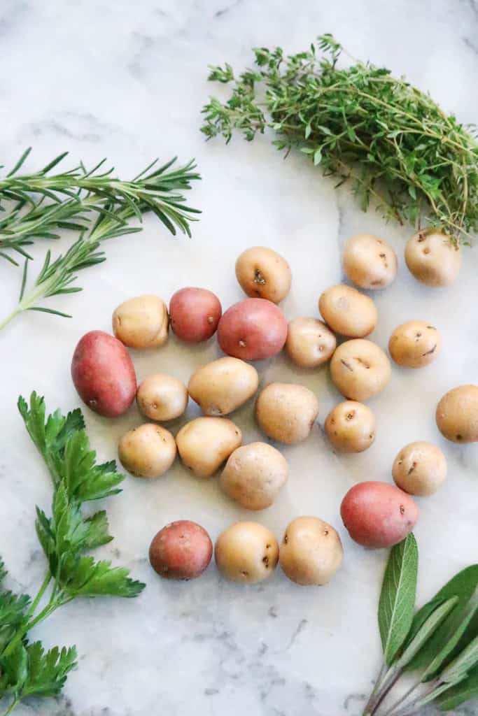 Overhead shot of red and white baby potatoes with fresh herb sprigs surrounding.