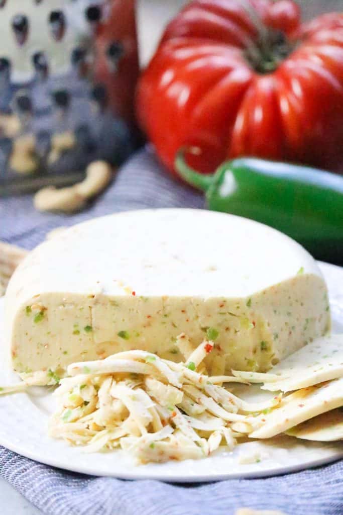 Side shot of vegan pepper jack cheese block shredded with pepper beside