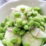 A serving of Asian cucumber salad in double white bowls with edamame and red onion.