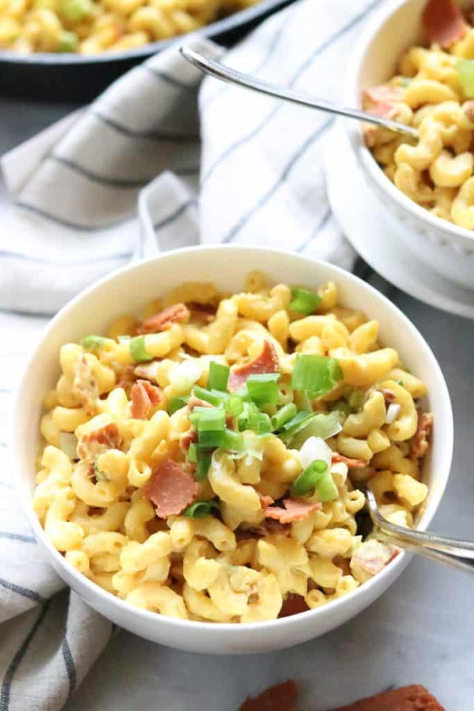 Two bowls of vegan mac and cheese garnished with vegan bacon and green onions.