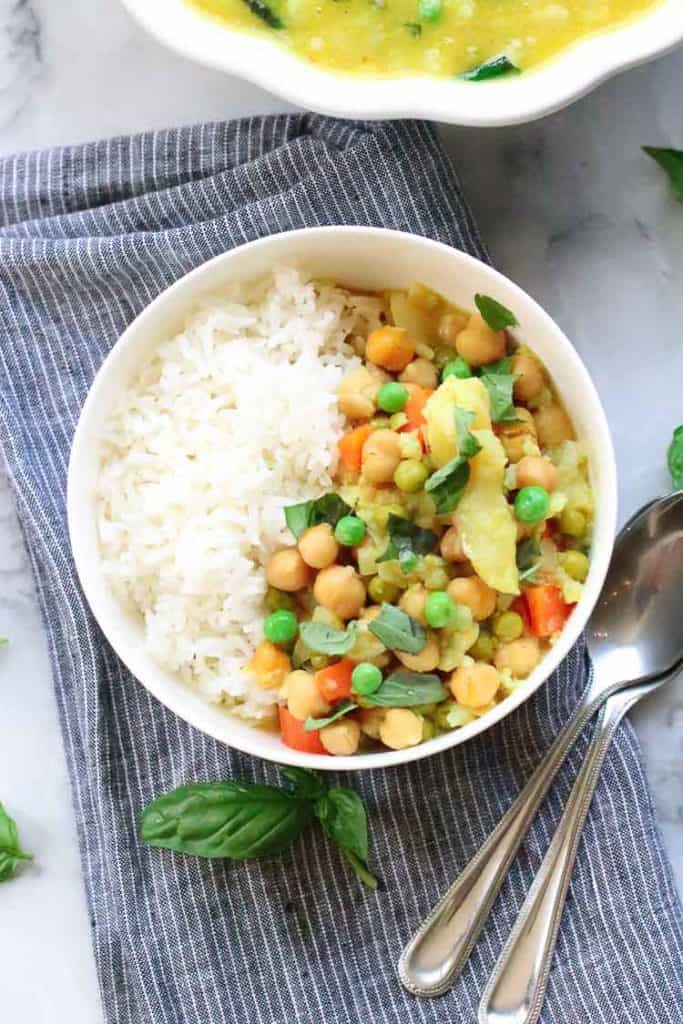 Closeup view of rice and vegan chickpea cauliflower curry in bowl with garnish of basil.