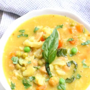 Overhead view of Chickpea and Cauliflower Curry in white bowl with garnish of fresh basil.