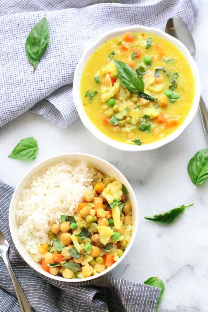 Overhead view of Chickpea Cauliflower Curry in bowls with basil leaves strewn around.