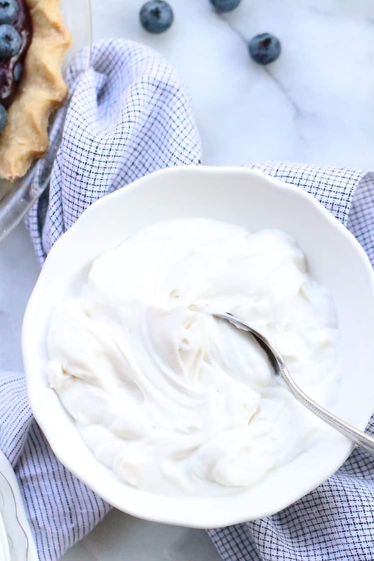 Overhead shot of vegan coconut whip cream in a white bowl with blueberries beside.