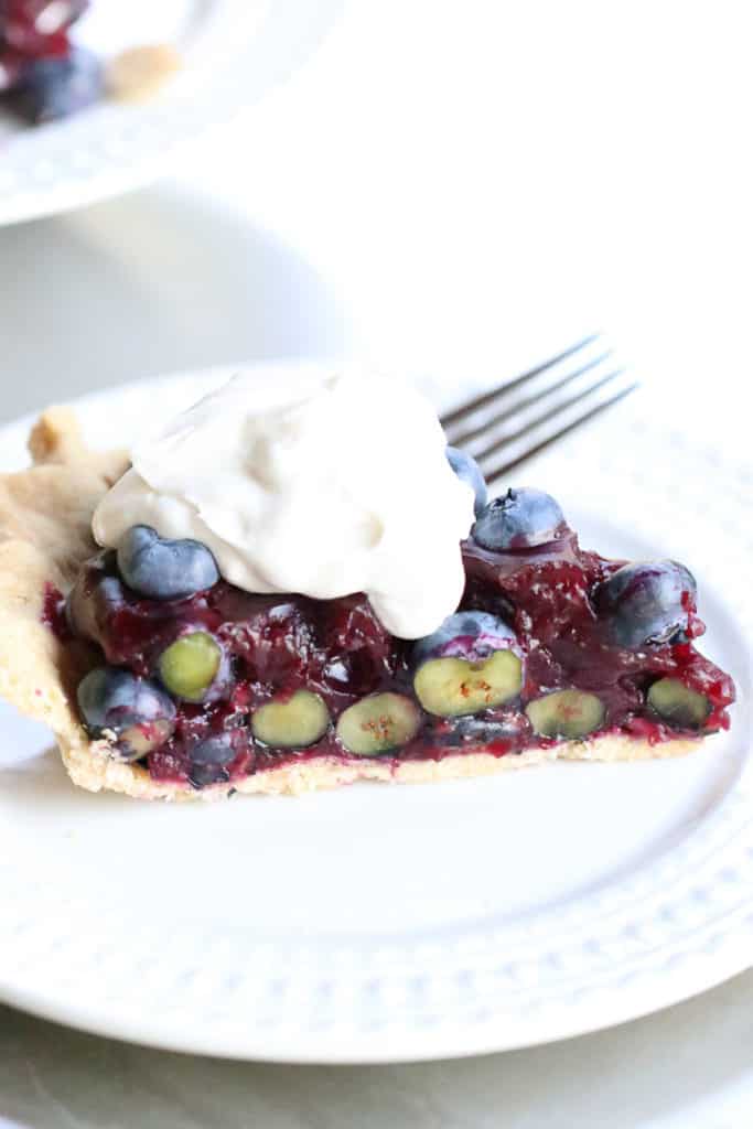 Side shot of easy blueberry pie with vegan whip cream on top on a white plate