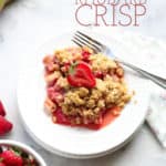servering af vegansk Rabarber Crisp på en hvid plade med gaffel og skiver jordbær