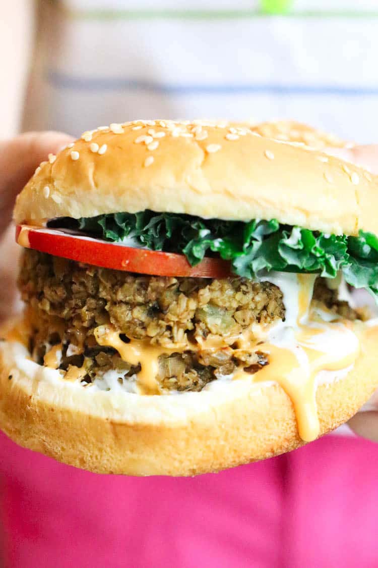 side shot of someone holding vegan oatmeal burger with sauces dripping