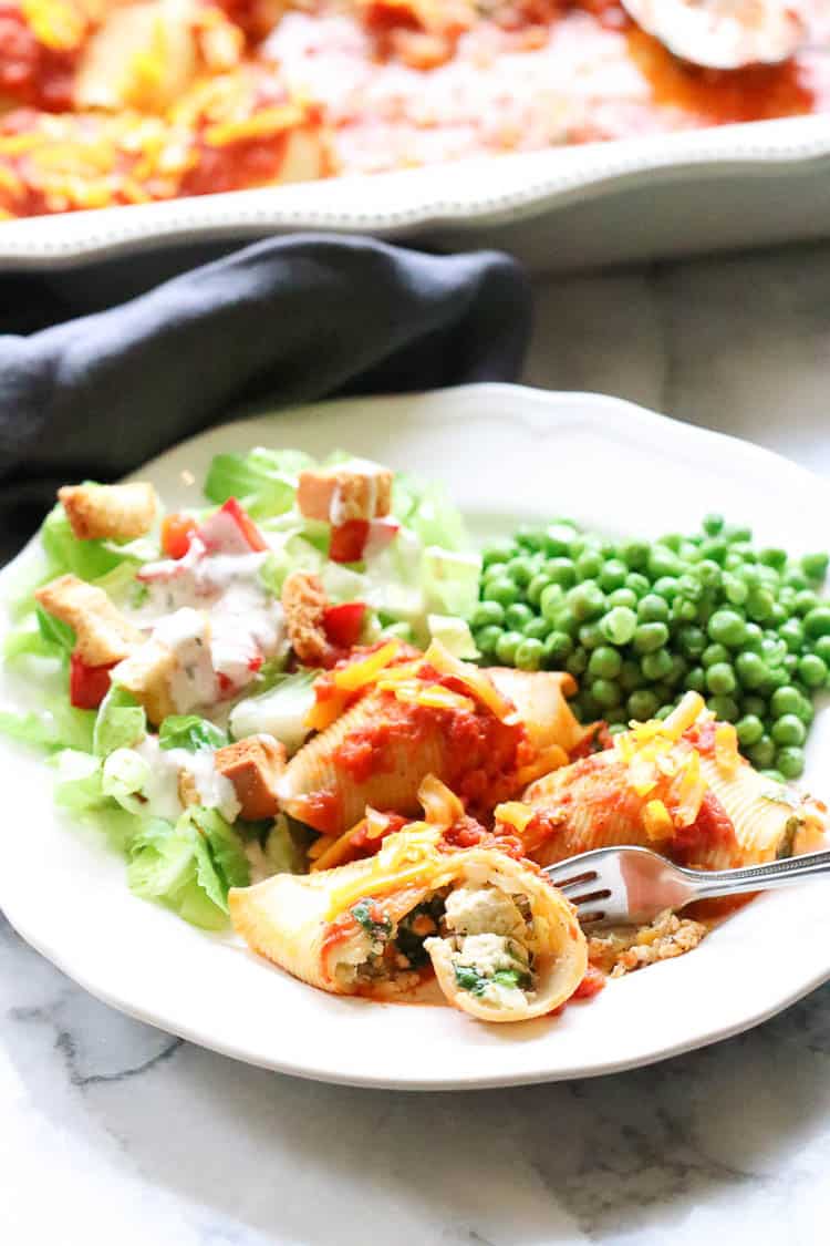 Vegan stuffed shells on a white plate with peas and salad.