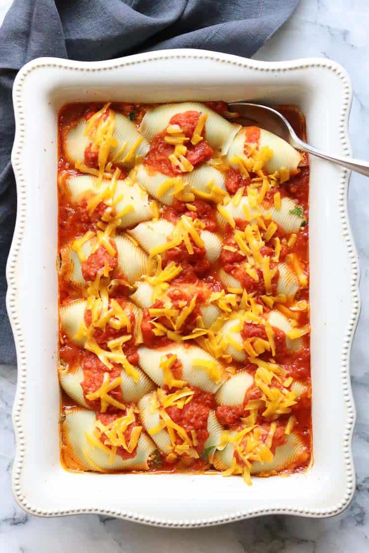 Vegan stuffed shells topped with vegan cheese in a white baking pan.