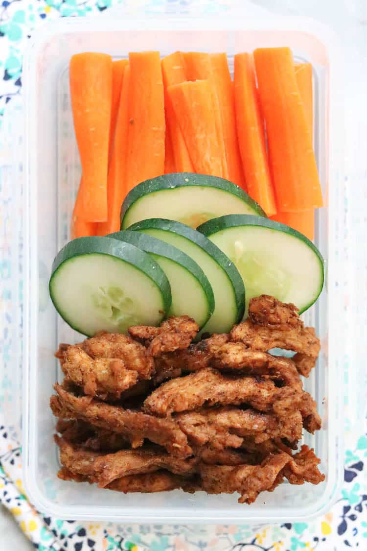 Overhead shot of vegan jerky in a lunch container with sliced cucumbers and carrots