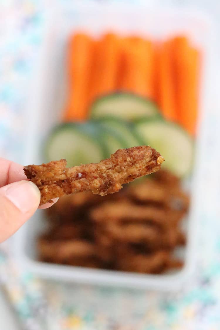 Closeup shot of a piece of vegan jerky with veggies and more jerky in the background.