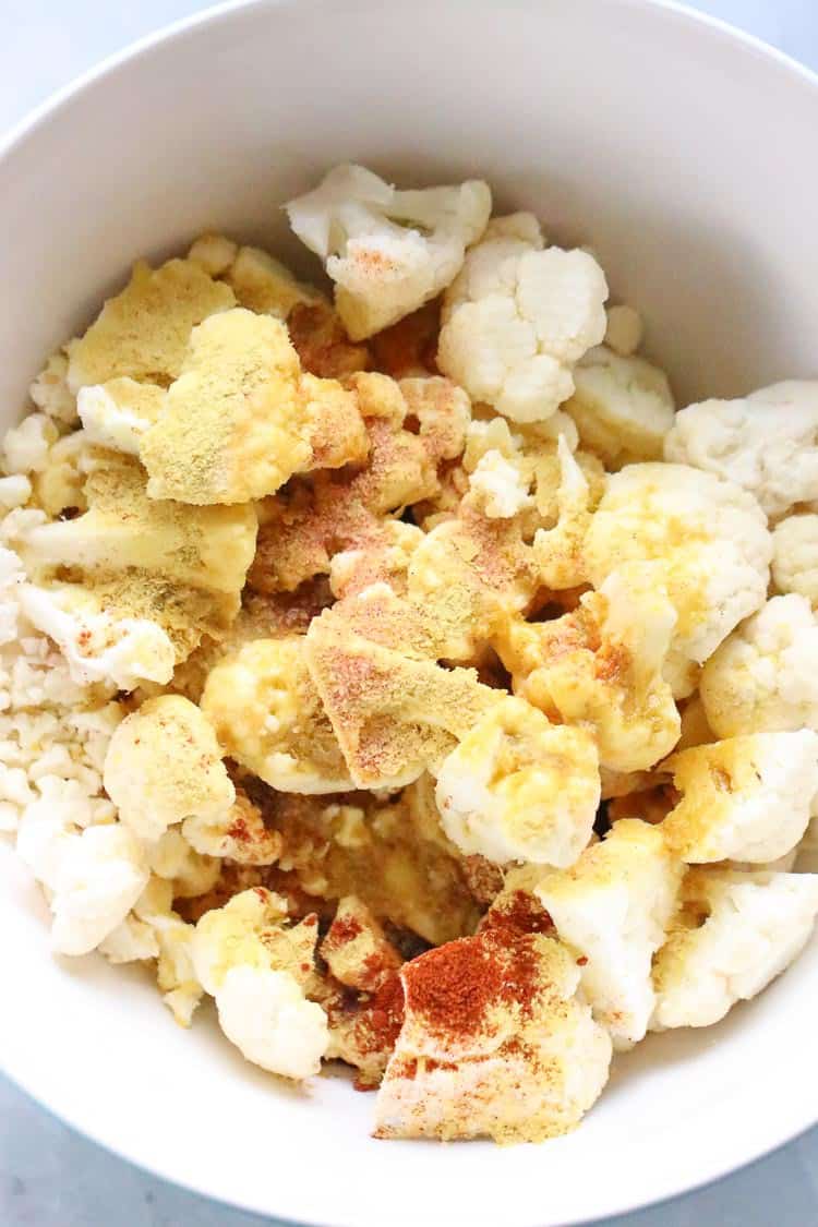 seasonings and olive oil sprinkled on cauliflower florets in a white bowl